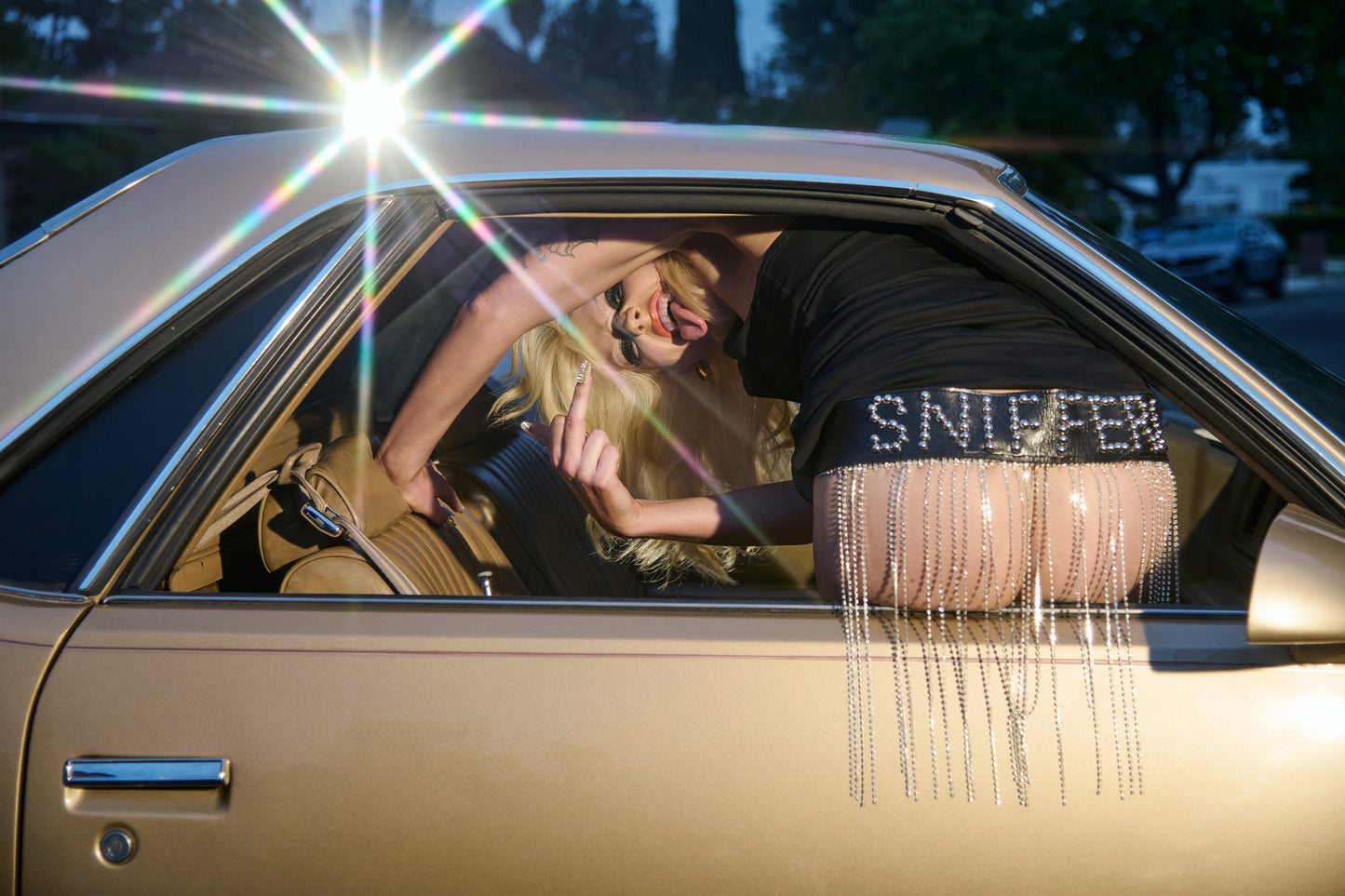 Amy Taylor of Amyl and the Sniffers sticking her tongue out, flipping off the camera, and showing her nude butt out of a car window with "sniffers" written on her leather belt.