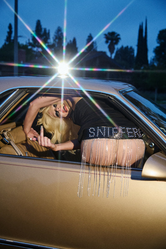 Punk woman, Amy Taylor of Amyl and the Sniffers revealing her buttocks out of a car window while also flipping the camera off.