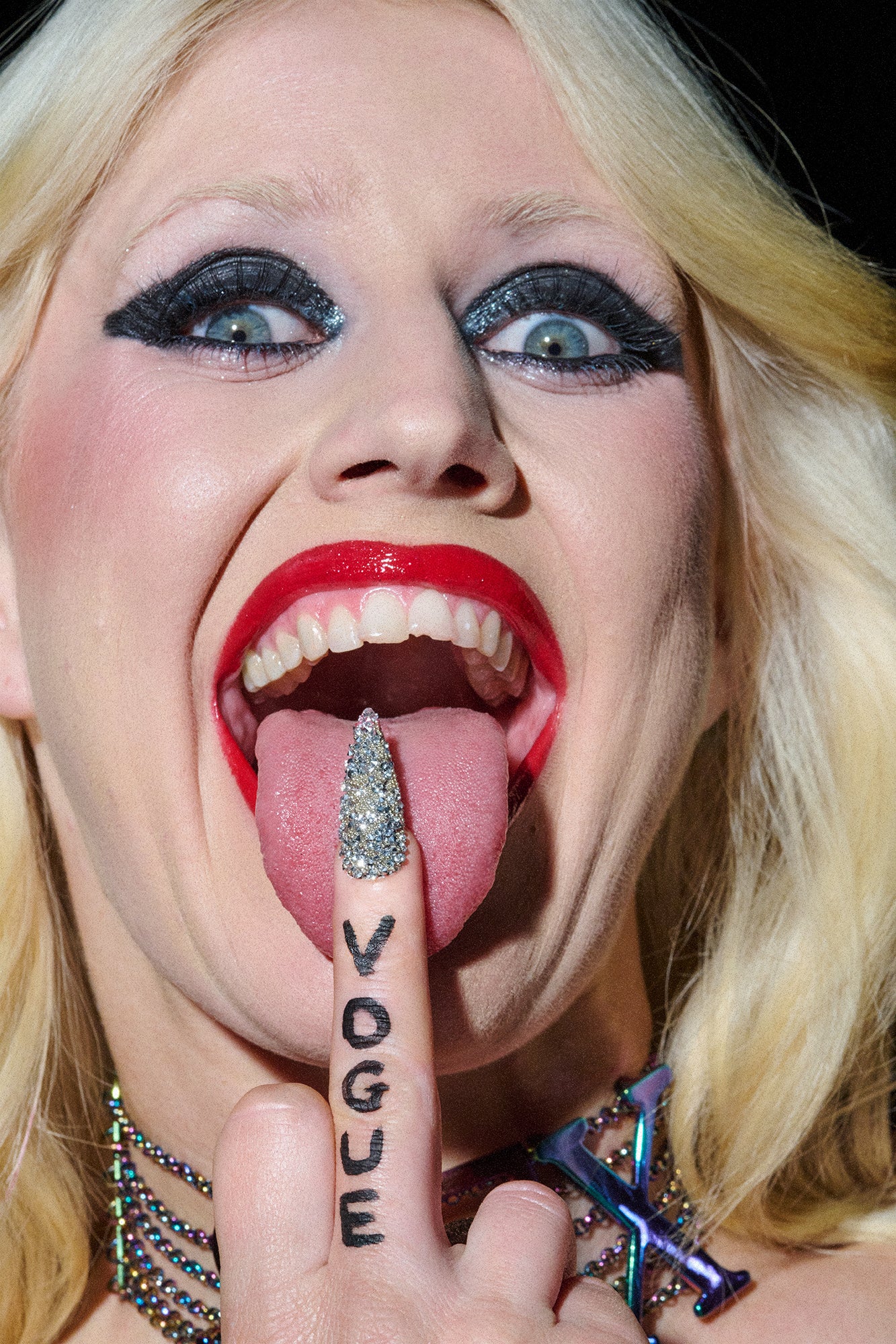 Close-up of a person with a finger in their mouth, wearing a ring and with 'Vogue' tattooed on their finger.