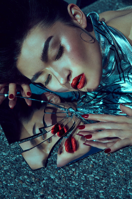 A artistic portrayal of an Asian woman's face reflected in a shattered mirror with pieces of glass around, predominantly in cool tones.