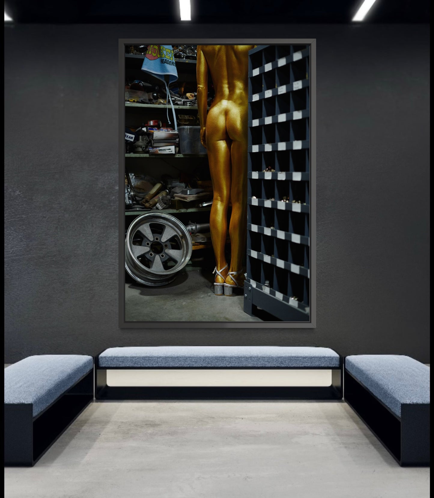 Gold painted nude woman in an industrial automotive repair shop room with shelves  and car parts.