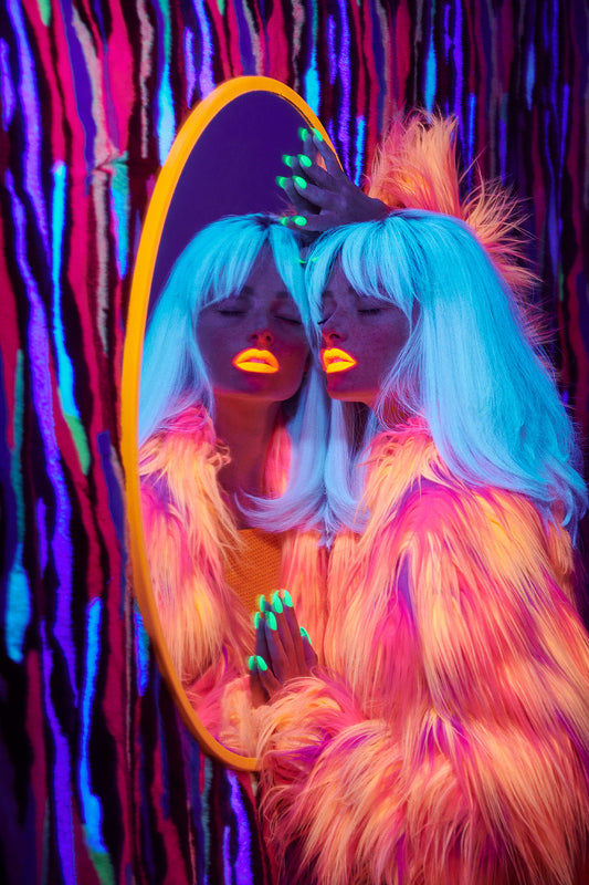 A vibrant fine art photograph featuring a person with blue neon hair and a fur coat, looking into a mirror with colorful lighting.