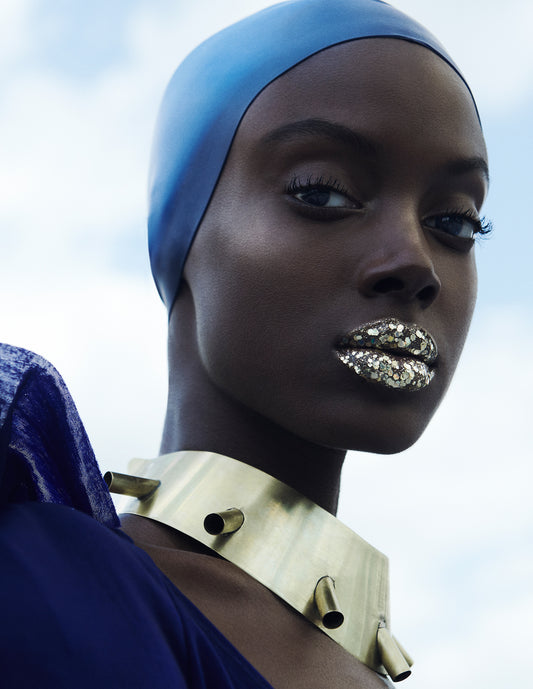 Black female model wearing blue swimming cap and gold chunky glitter lipstick and african necklace olympics beauty editorial