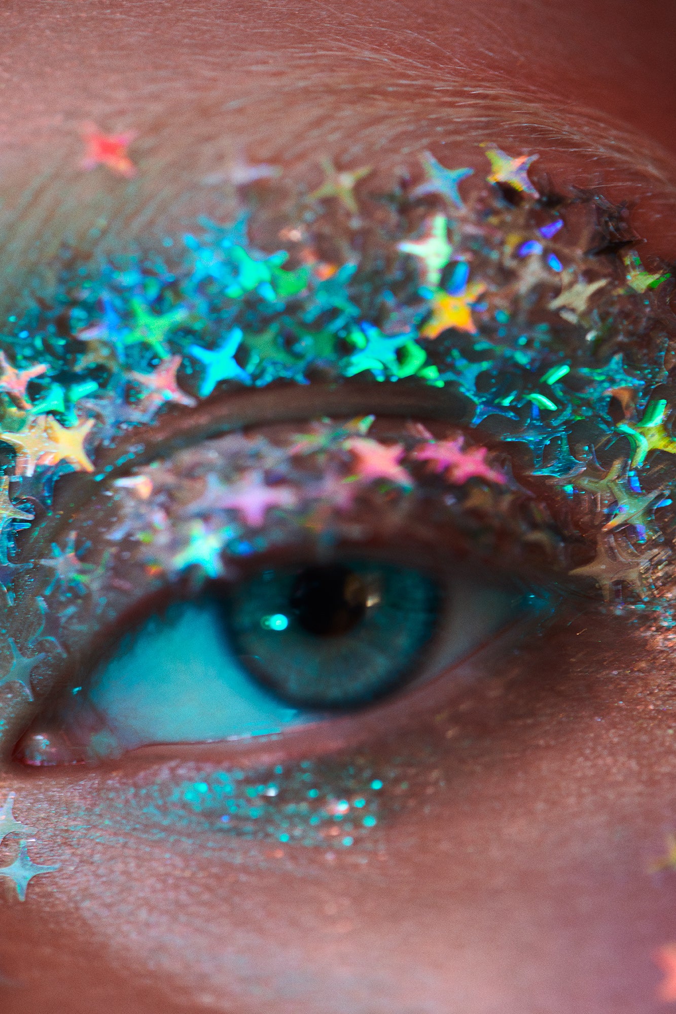 Close-up macro beauty editorial of woman with blue eyes with iridescent diamond and star shaped glitter on her eyelid and bleached eyebrows