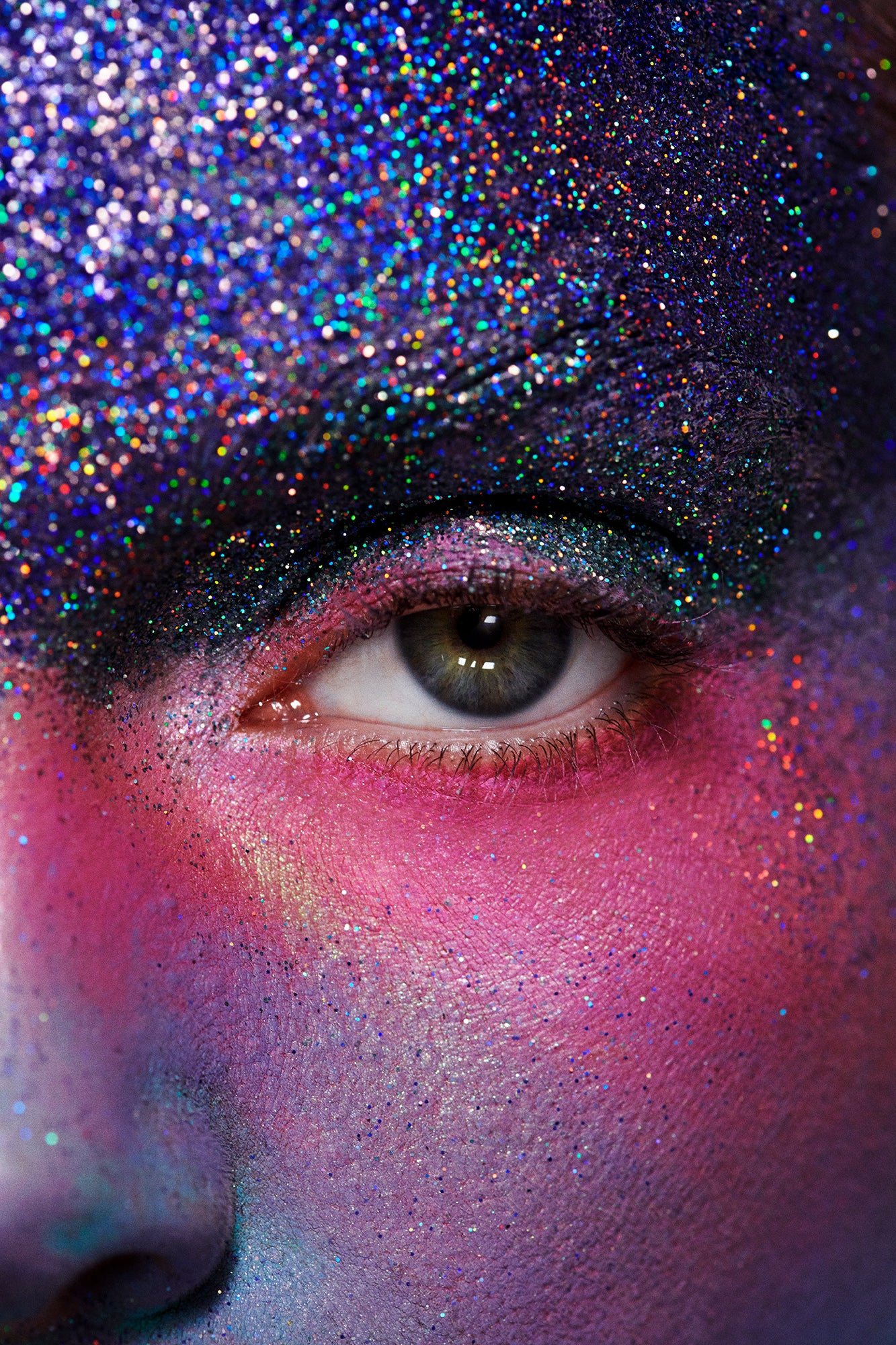 Extreme close up image of a woman's eye with blue glitter covering her eyebrow and pink and purple gradient makeup below the eye. Alien spacey futuristic creative makeup for a beauty magazine.