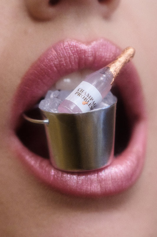 Close-up of woman's pink lips with a miniature bucket of ice and champagne bottle between her lips.