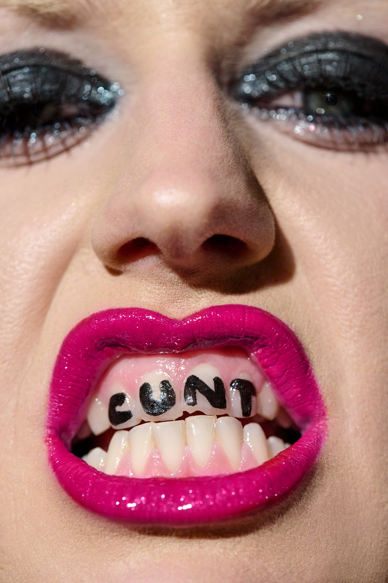 Close-up portrait of Amy of Amyl and the Sniffers with bright pink lipstick and the word 'CUNT' written on her teeth.
