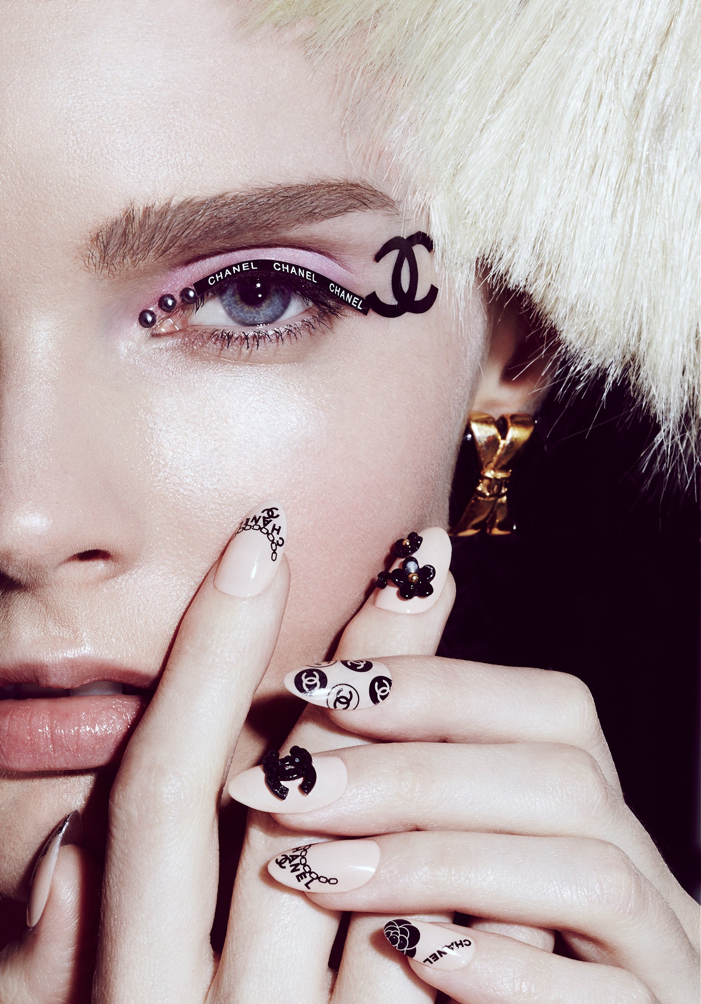 Close up macro of woman wearing chanel logo eyeliner face stickers and chanel fingernails manicure