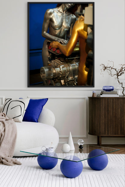 A modern living room with abstract art of two nude female mechanics working on a big block car engine. The room also has blue spherical ottomans and a glass coffee table.