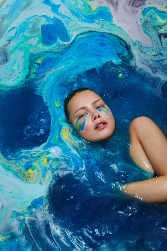 Fine art photo of worldly earthy pollution waste ecologically concerned woman in a bath of blue and yellow swirls from a colorful bath bomb. Appears to be a topographical map of earth shot from space