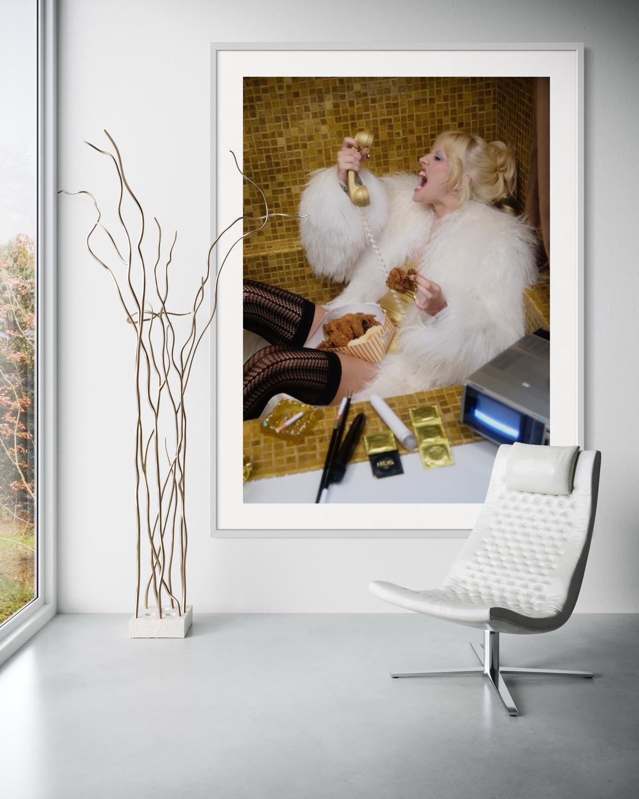 Framed artwork of Amy Taylor (singer of Amyl and the Sniffers band) wearing a fur coat sitting in a gold tiled bath tub as she eats fried chicken and screams into a vintage telephone.