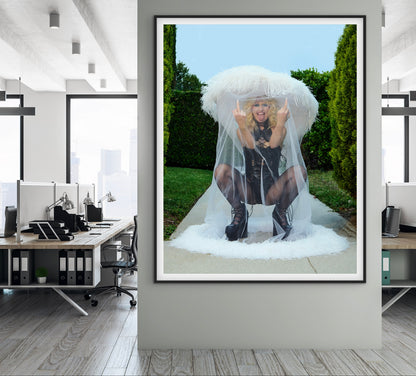 Amy Taylor of Amyl and the Sniffers flipping off camera wearing large veiled hat and custom Zana Bayne bondage punk black leather outfit in a garden setting.