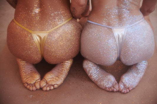 Two women sitting with bikini bums covered in silver and gold glitter trend beach sand