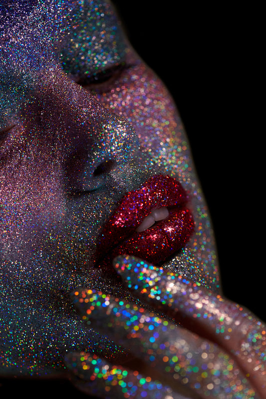 Close-up of a person's face and hands covered in multicolored glitter, with a focus on the shiny, sparkling makeup.