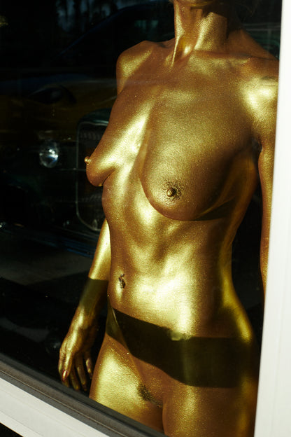 Am artistic image shot through a window of a Goldfinger Bond style girl's torso and breasts as the sun hits floods through.