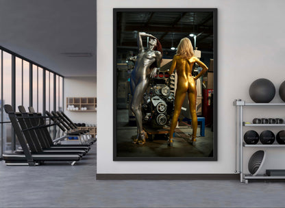 Framed artwork of two nude women in Rosie the Riveter style located in an auto body shop with a large supercharged engine.