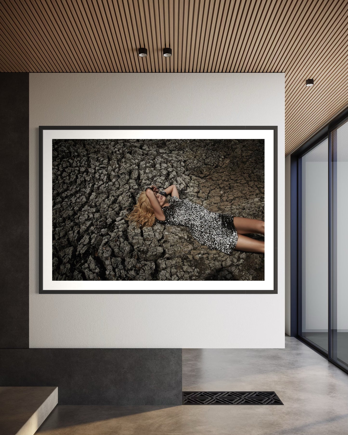 Framed photograph of a person lying on a textured surface in a modern interior setting.