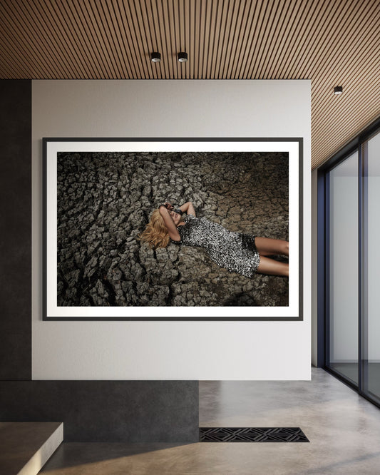 Framed photograph of a person lying on a textured surface in a modern interior setting.