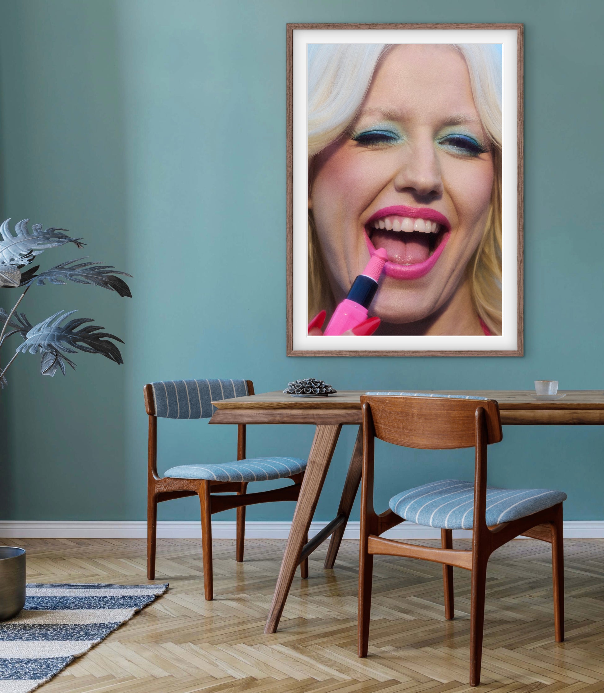 A blue dining room with a large framed art photo of punk singer Amy Taylor (Amyl and the Sniffers) winking and smiling while applying lipstick. The photograph is by renowned photographer Jamie Nelson.