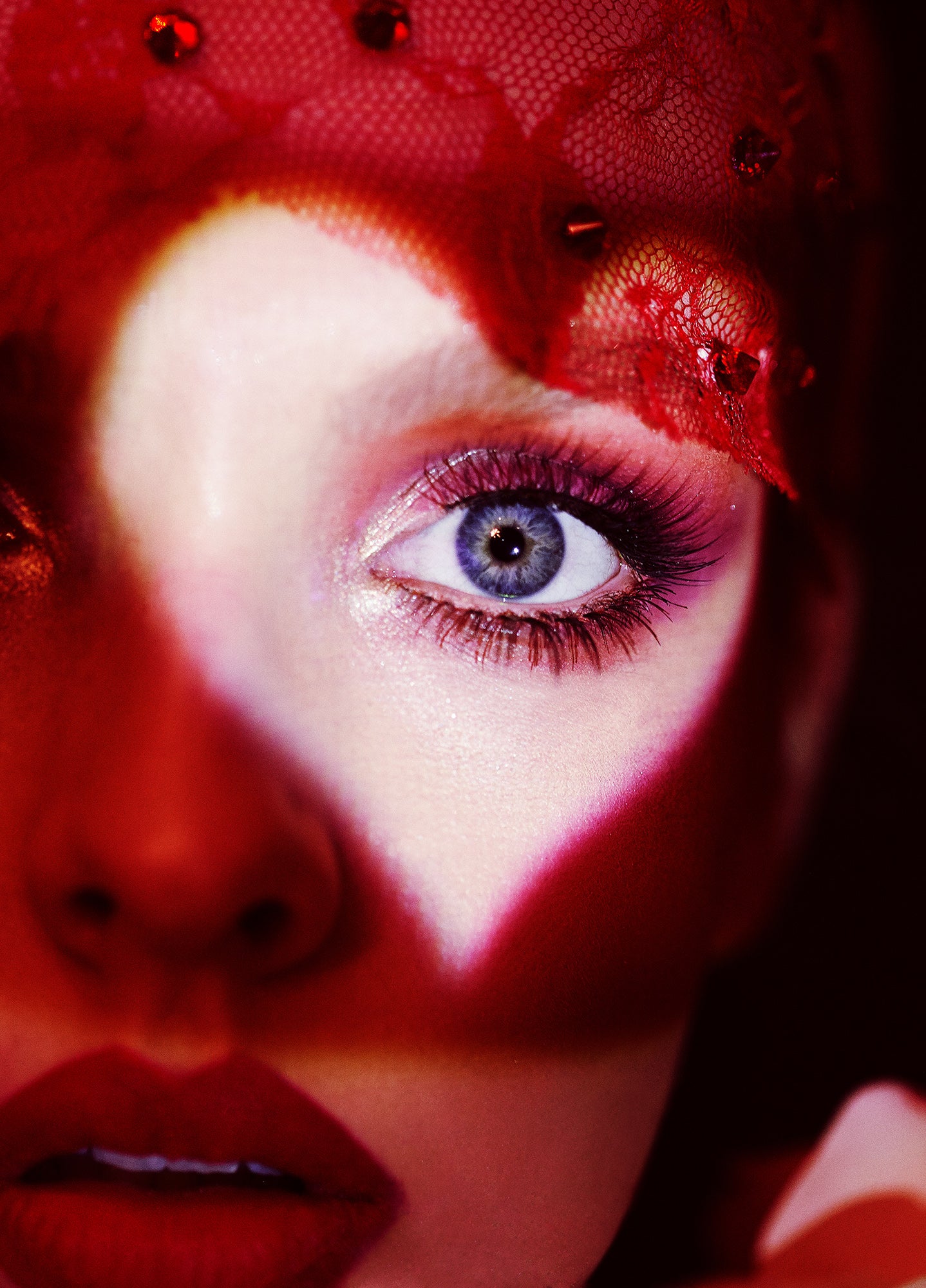 beauty editorial of woman with long eyelashes with heart projection spotlight around her eye wearing lace veil with red light surrounding her 