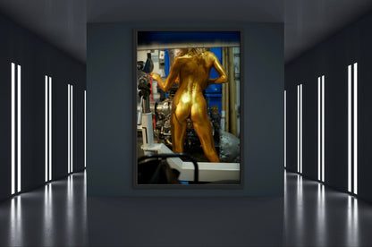 Framed artwork of an athletic woman who is nude and painted entirely gold  working with machinery  in an industrial setting.