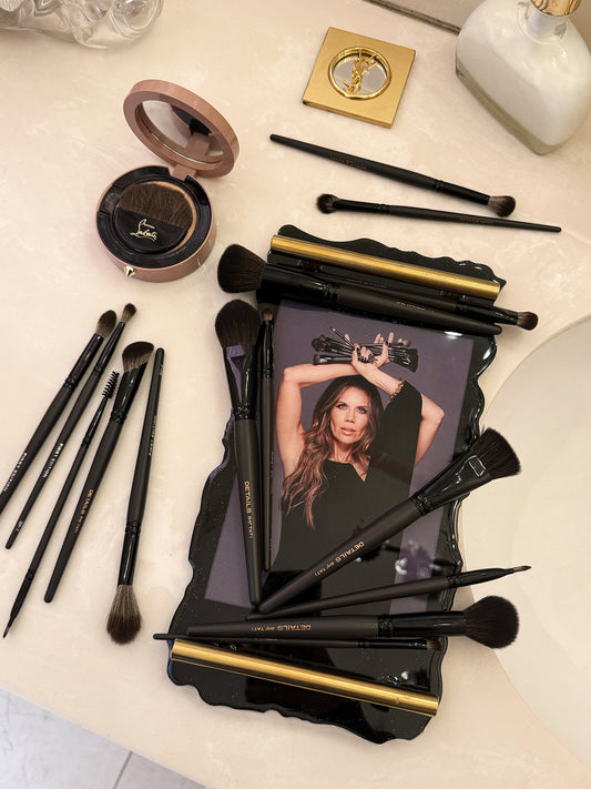 Makeup brushes and a compact mirror on a light surface with a magazine featuring a woman.
