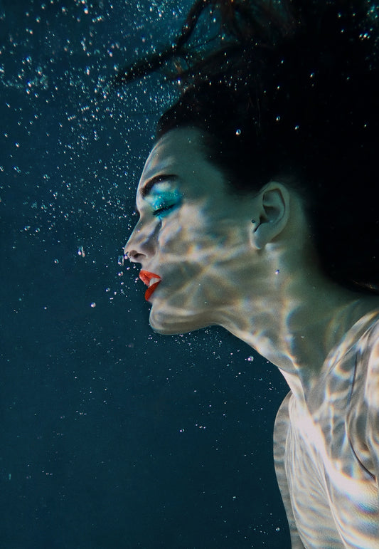 Girl female model underwater wearing blue eyeshadow red lipstick breathing bubbles peaceful serene blue fine art. 