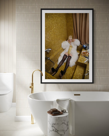 Framed artwork of woman laying in gold tiled vintage sunken bath tub.