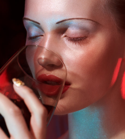 Woman with 20's and 40's style thin pencil eyebrows drinks wine with red light on her face holiday christmas beauty editorials