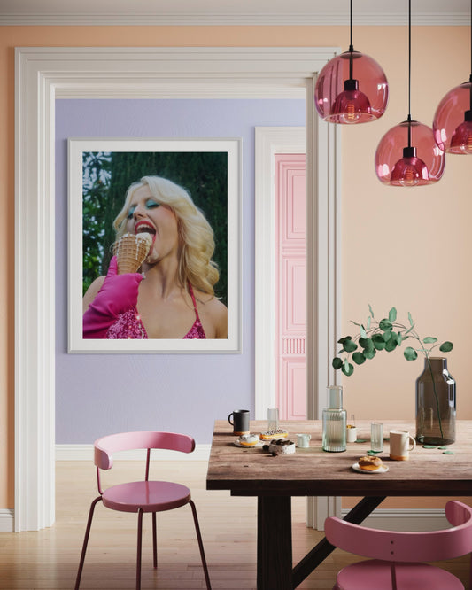 Dining room with a framed picture of a woman eating ice cream, pink chairs, and pink pendant lights.