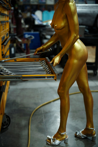 Gold-colored statue of a nude figure with silver shoes in a workshop setting.