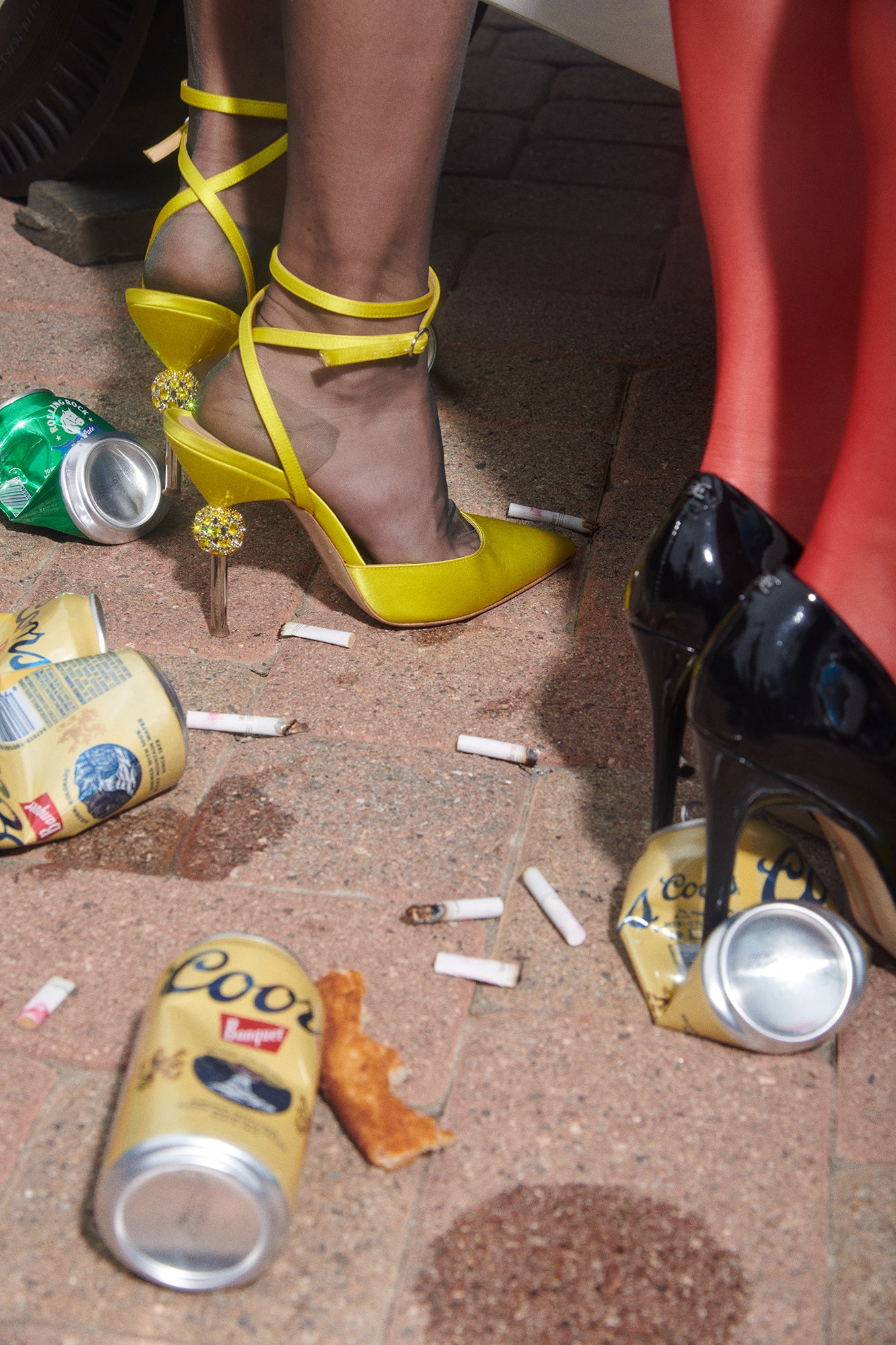 Art print of close-up of womens 80s style heels standing on a messy street. An after party with trash, beer cans, cigarette butts, and pizza on new york city street